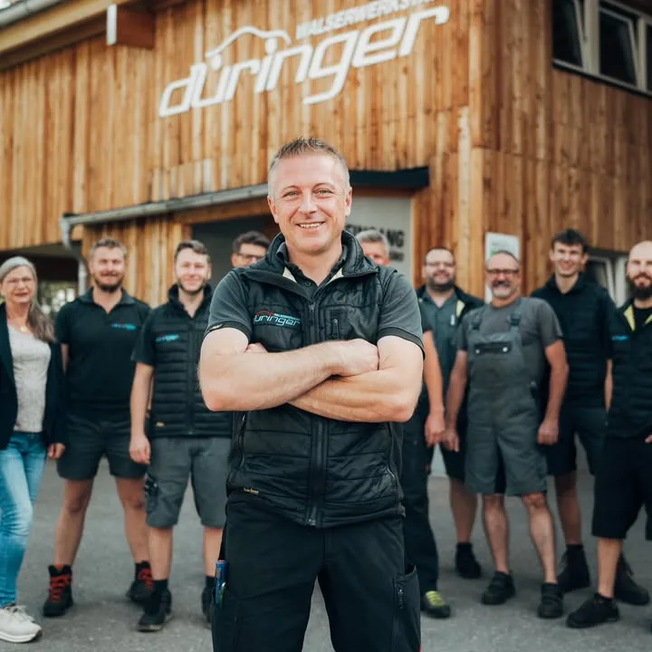 Die Mannschaft der Walserwerkstatt Düringer vor der Werkstatt, darüber das Firmenschild